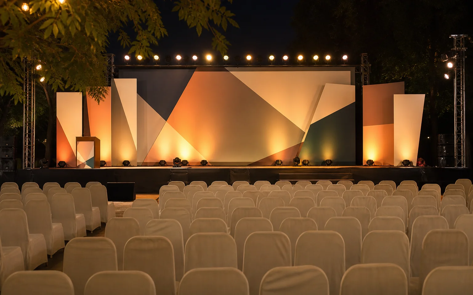A warmly lit event stage in an Indian hall with seating and a geometric backdrop