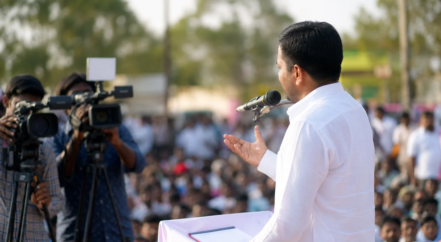 A camera crew filming a public speaker from the side at an outdoor gathering